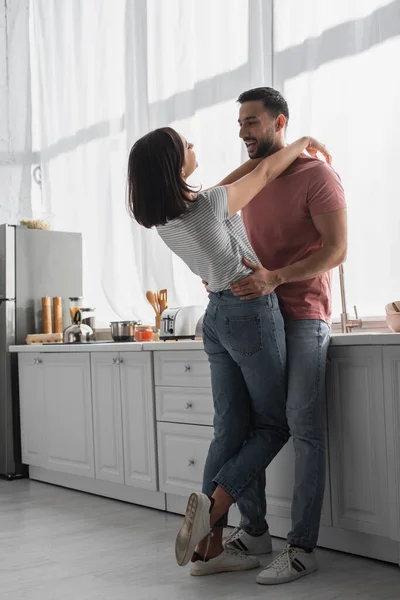 Позитивная молодая женщина обнимает парня с руками на плечах на кухне — стоковое фото