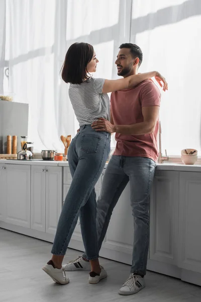 Feliz joven mujer abrazando novio con las manos en los hombros en la cocina - foto de stock