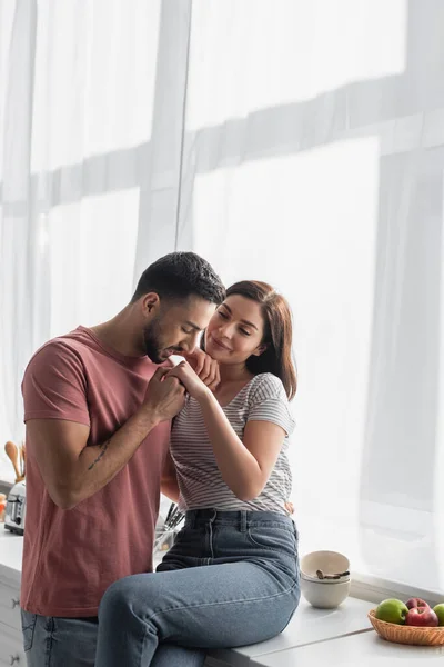 Jovem com os olhos fechados beijando a mão da namorada na cozinha — Fotografia de Stock