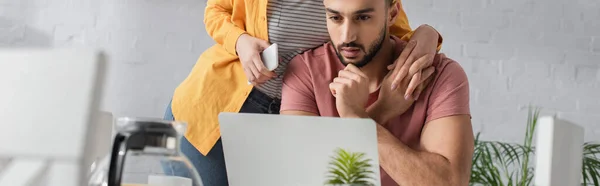Young woman holding cellphone and touching hands with boyfriend working with laptop at home, banner — Stock Photo
