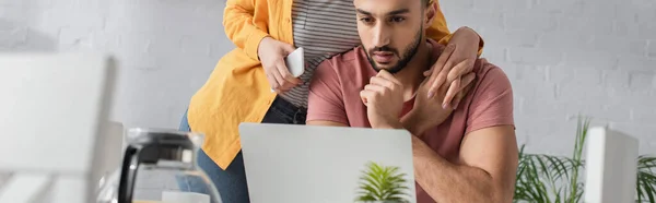 Jeune femme tenant son téléphone portable et touchant les mains avec son petit ami travaillant avec un ordinateur portable à la maison, bannière — Photo de stock