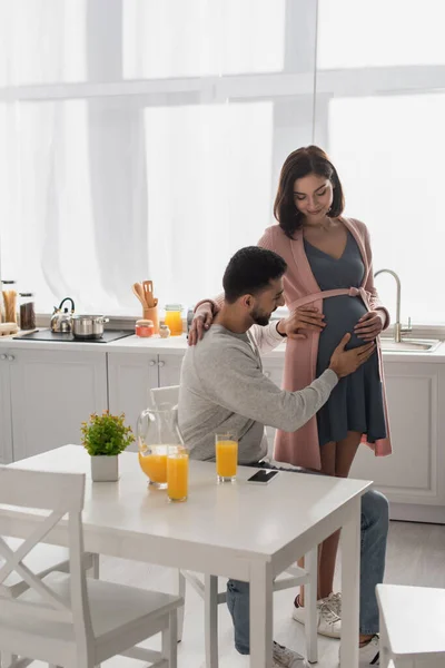Young man touching belly of pregnant woman in kitchen — Stock Photo