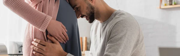 Junger Mann berührt Bauch einer Schwangeren mit Kopf in Küche, Banner — Stockfoto
