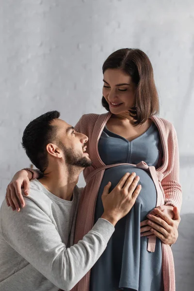 Jovem gentilmente abraçando a barriga da mulher grávida na cozinha — Fotografia de Stock