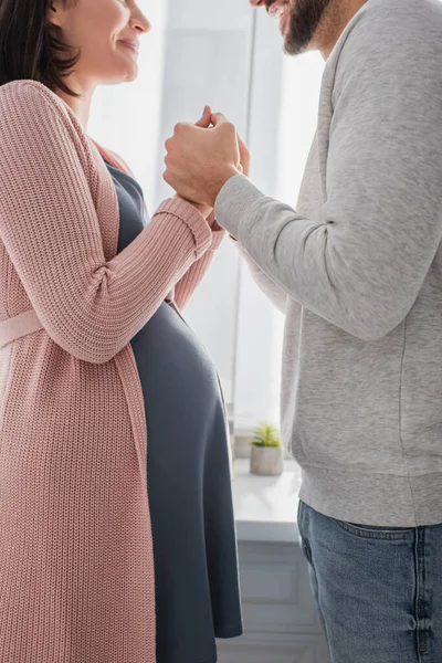 Частичный взгляд молодого человека, держащегося за руки с беременной женщиной на кухне — стоковое фото