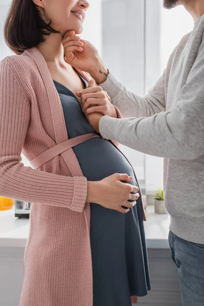 Teilbild eines jungen Mannes, der Gesicht und Hand einer schwangeren Frau zu Hause behutsam hält — Stockfoto