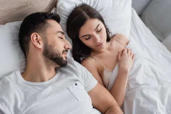 Высокий угол обзора молодой пары, спящей на белом белье в спальне — стоковое фото