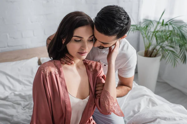 Junger Mann berührt Freundin in Peignoir im Schlafzimmer am Hals — Stockfoto