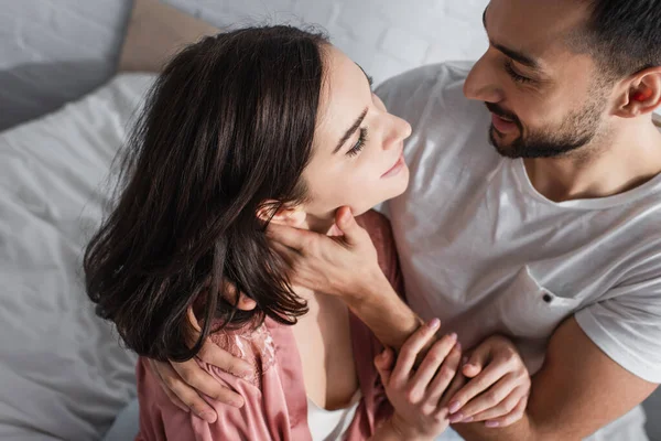 Vue grand angle de jeune femme souriante dans peignoir étreignant avec petit ami sur le lit dans la chambre — Photo de stock