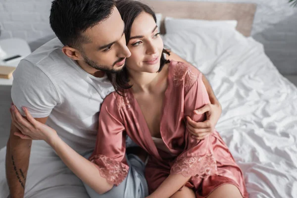 Vista de ángulo alto de la joven pareja sonriente abrazándose suavemente en el dormitorio - foto de stock