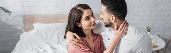 Lächelndes junges Paar, das sich sanft umarmt und einander im Schlafzimmer ansieht, Banner — Stockfoto