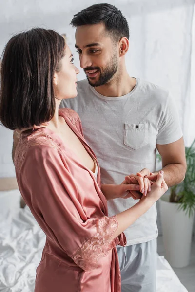 Sorridente giovane coppia tenendosi per mano e guardandosi in camera da letto — Foto stock