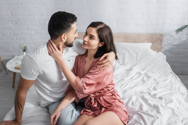 Glückliches junges Paar, das sich im Schlafzimmer sanft umarmt und anschaut — Stockfoto