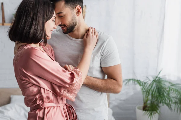 Feliz joven pareja gentilmente abrazando con los ojos cerrados en el dormitorio - foto de stock