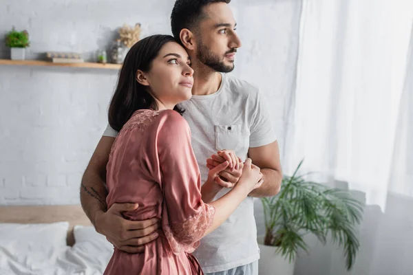 Glückliches junges Paar, das sich sanft umarmt und Händchen hält im Schlafzimmer — Stockfoto