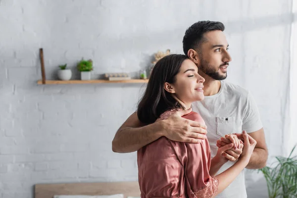 Sorrindo jovem casal gentilmente abraçando e de mãos dadas no quarto — Fotografia de Stock