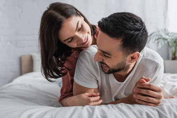 Lächelndes junges Paar liegt mit weißer Bettwäsche auf dem Bett und umarmt sich im Schlafzimmer — Stockfoto