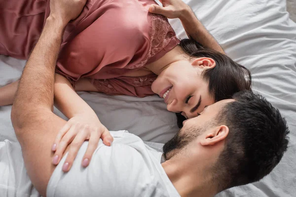 Vista superior do jovem deitado na cama com linho branco e gentilmente abraçando namorada no quarto — Fotografia de Stock