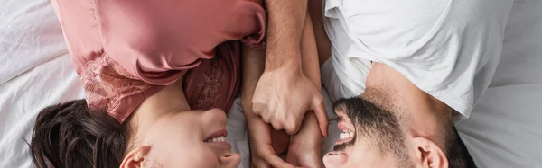 Vue du dessus du jeune homme couché sur le lit avec du linge blanc et tenant doucement les mains de la petite amie dans la chambre, bannière — Photo de stock