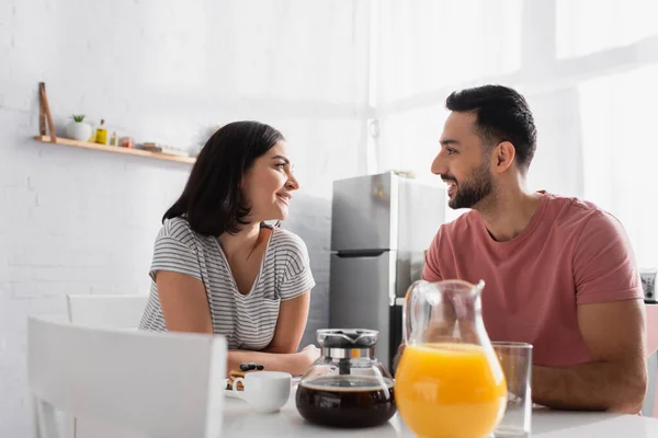 Heureux jeune couple assis à table avec petit déjeuner, café et jus d'orange dans la cuisine — Photo de stock