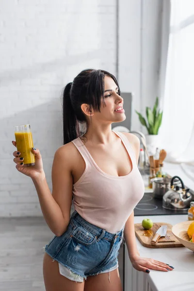 Happy young woman holding glass of smoothie in kitchen — Stock Photo