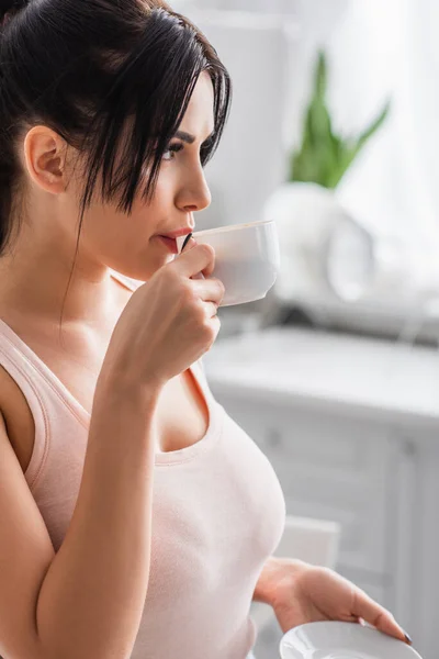 Молода брюнетка жінка п'є каву на кухні — стокове фото