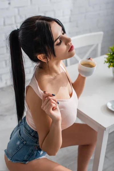 Alto ángulo vista de joven morena mujer sosteniendo taza de café - foto de stock
