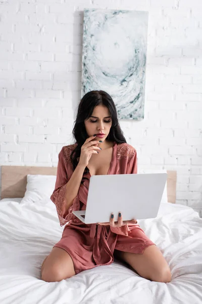 Junge Frau im Seidenmantel hält Laptop im Schlafzimmer — Stockfoto