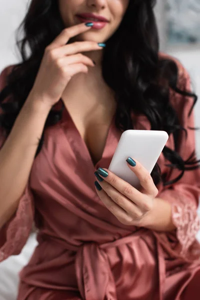 Cropped view of smiling woman in silk robe using smartphone — Stock Photo