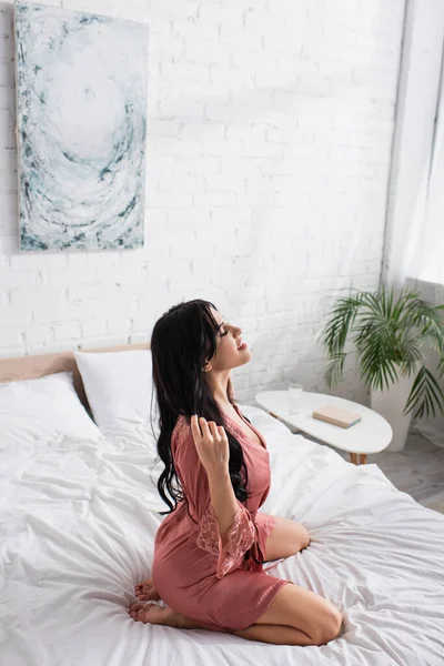 High angle view of happy young woman in silk robe sitting on bed — Stock Photo