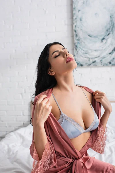 Чуттєва молода жінка в сексуальному бюстгальтері знімає шовковий халат — Stock Photo