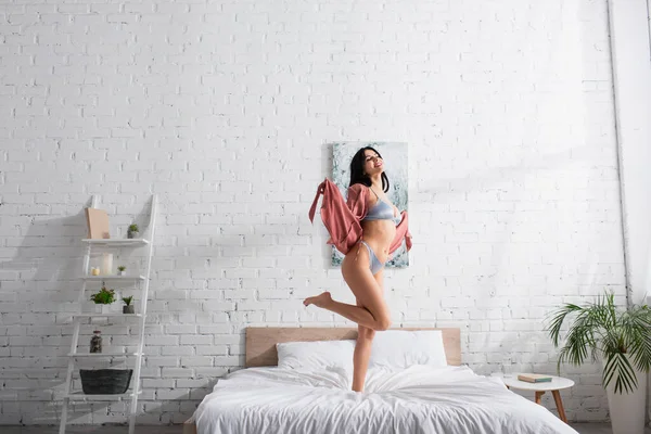A piedi nudi e felice donna in biancheria intima sexy in piedi sul letto — Foto stock