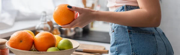 Vista cortada de jovem segurando laranja madura na cozinha, banner — Fotografia de Stock