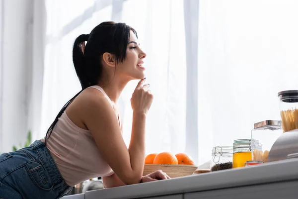 Happy young and brunette woman looking away in kitchen — Stock Photo