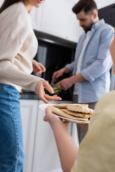 Girl holding plate with fried chicken fillet near blurred parents preparing breakfast — Stock Photo