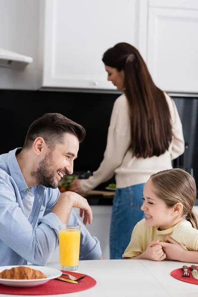 Felice padre e figlia ridendo durante la colazione in cucina vicino alla madre offuscata — Foto stock