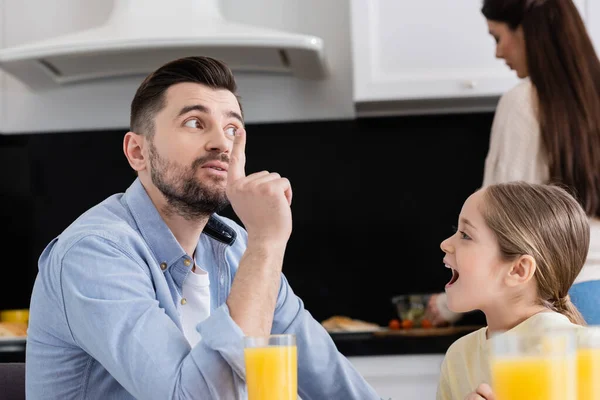 Homme montrant geste idée près de fille étonnée et femme floue préparer le petit déjeuner — Photo de stock