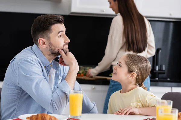 Cheerful child looking at thoughtful dad near breakfast and blurred mother in kitchen — Stock Photo