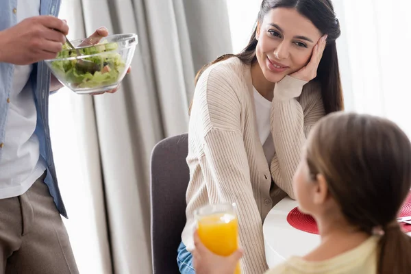 Vue arrière de l'enfant flou tenant du jus d'orange près de maman et papa heureux avec salade de légumes — Photo de stock