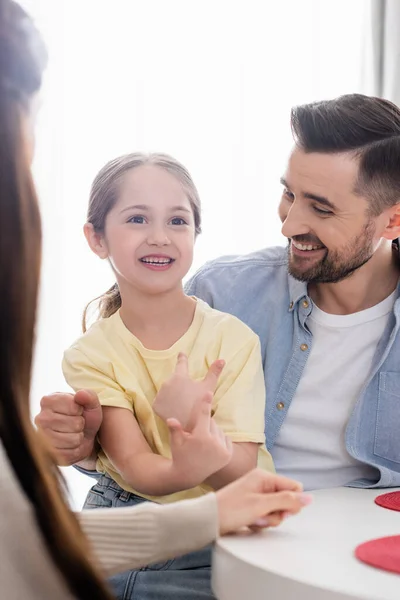 Fröhliches Mädchen gestikuliert im Gespräch mit glücklichen Eltern zu Hause — Stockfoto