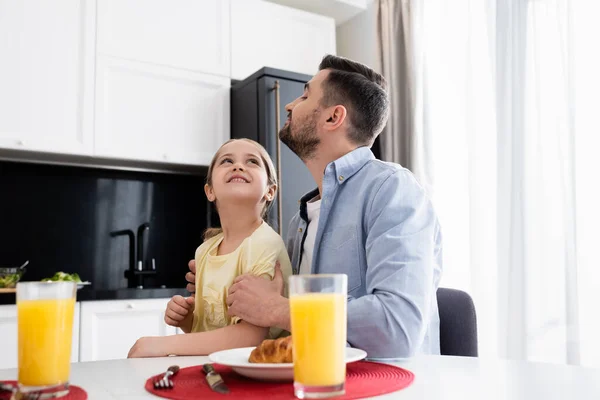 Pai feliz e filha olhando um para o outro perto do café da manhã na cozinha — Fotografia de Stock