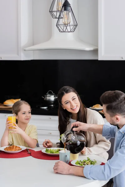 Чоловік наливає каву біля радісної дружини і дочки з апельсиновим соком — стокове фото