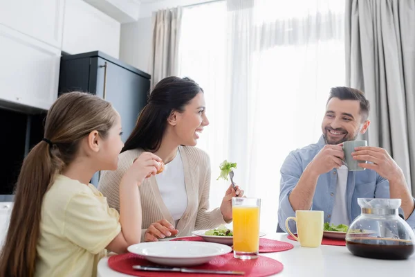 Couple joyeux souriant pendant le petit déjeuner avec fille dans la cuisine — Photo de stock