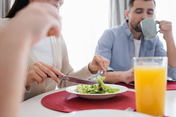 Woman eating vegetable salad near blurred husband and daughter in kitchen — Stock Photo