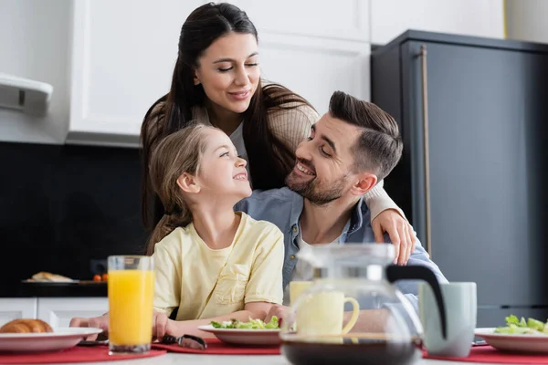 Happy family smiling near breakfast in kitchen on blurred foreground — Stock Photo