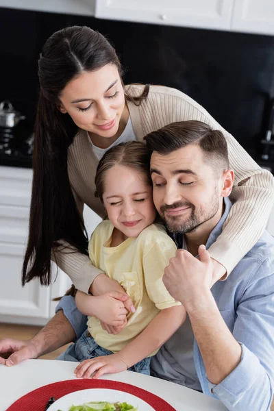 Cheerful couple with daughter embracing in kitchen during breakfast — Stock Photo