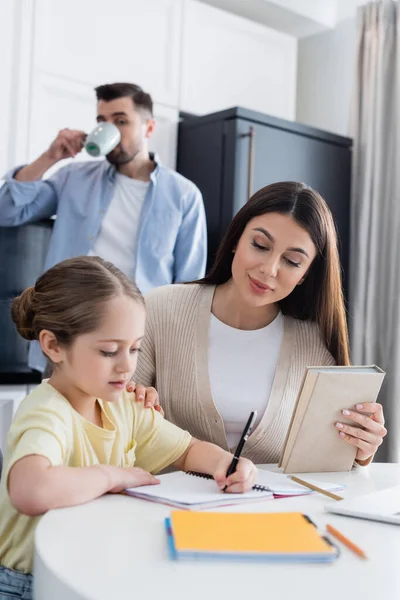 Mann trinkt Kaffee in der Nähe der Tochter und macht Hausaufgaben mit Mutter — Stockfoto