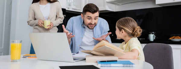 Hombre excitado gesto mientras ayuda a su hija haciendo la tarea cerca de la esposa con una taza de café, pancarta - foto de stock