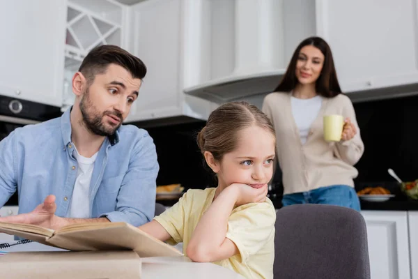 Man talking to offended daughter while doing homework near wife on blurred background — Stock Photo