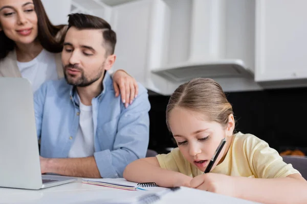 Mujer borrosa sonriendo cerca de marido e hija escribiendo en cuaderno - foto de stock